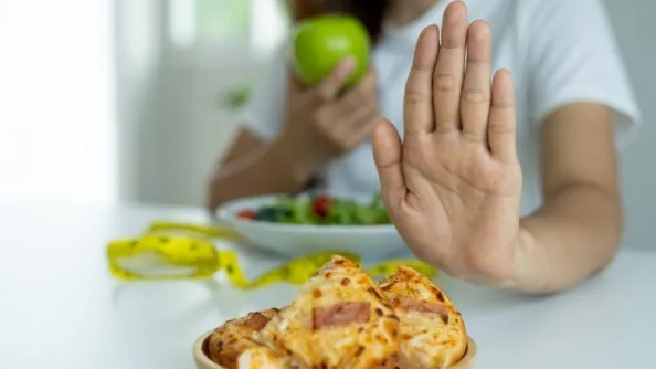 a woman showing avoid sign to the junk food while eating green food