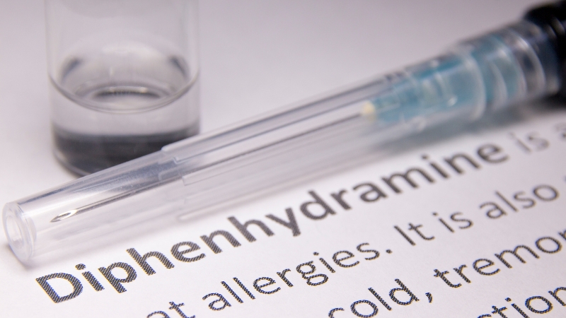syringe with a solution in a beaker is kept upon a sheet with the information of diphenhydramine